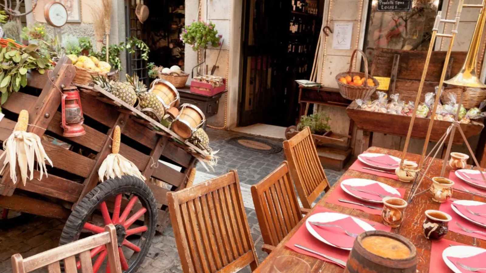 Rustic street-side table set with red napkins beside a wooden cart of fruit and corn cobs