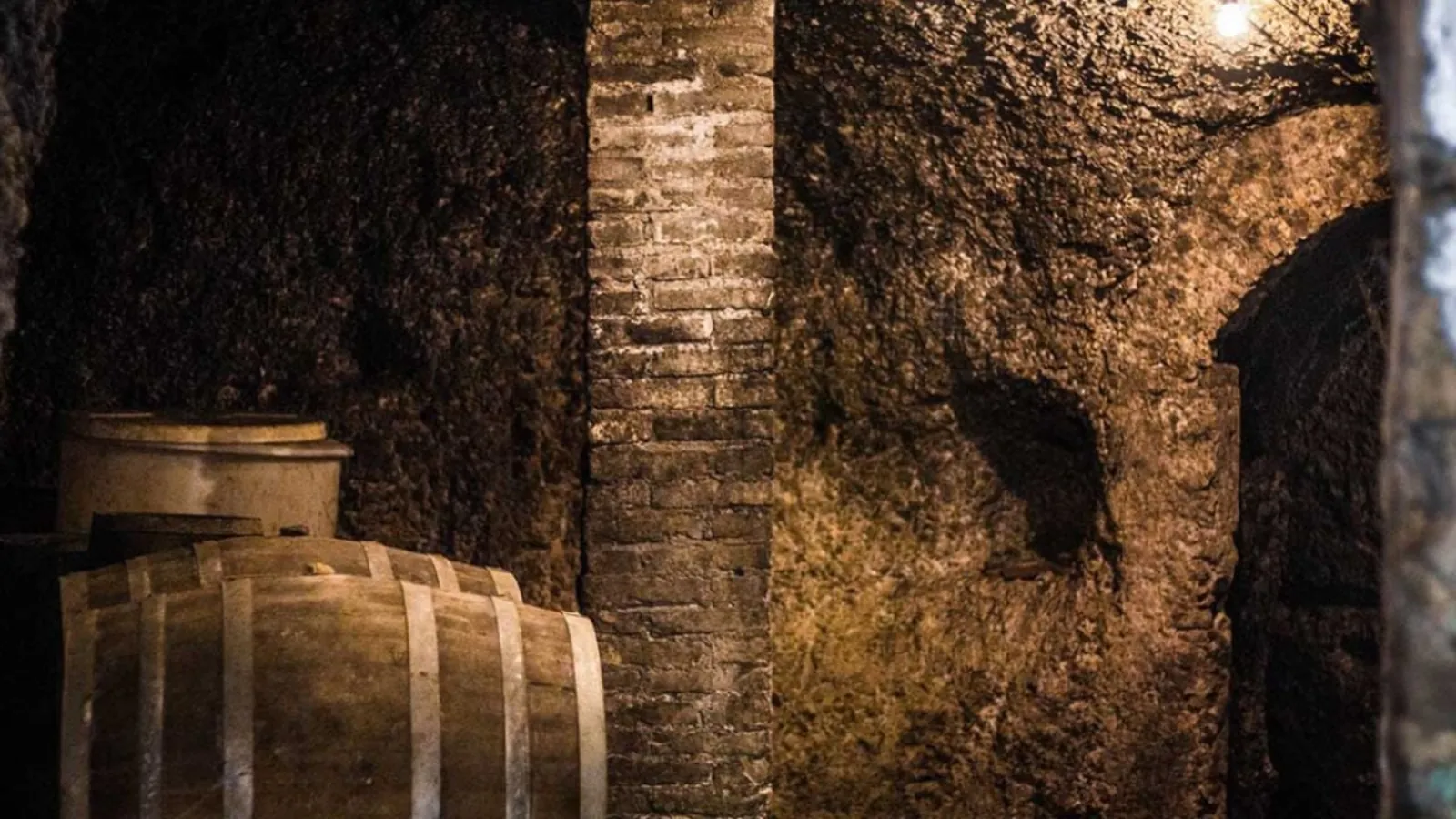 Wine barrels in a dim tufa cellar with a brick pillar