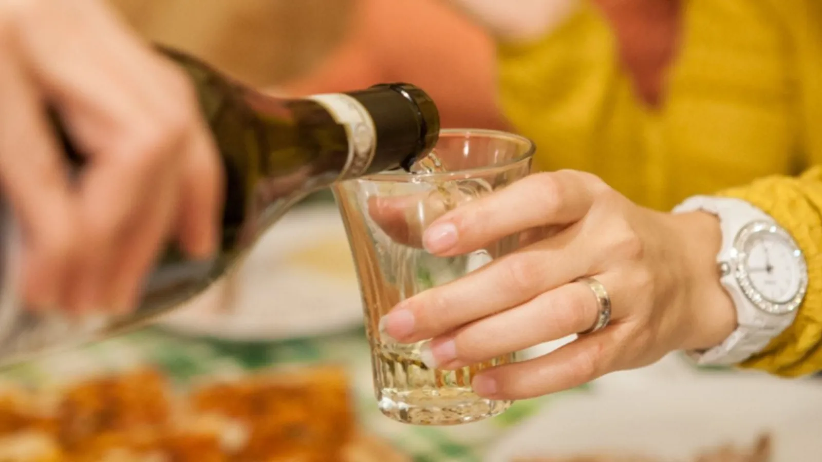 Hand pouring white wine from a bottle into a small glass at a lunch table