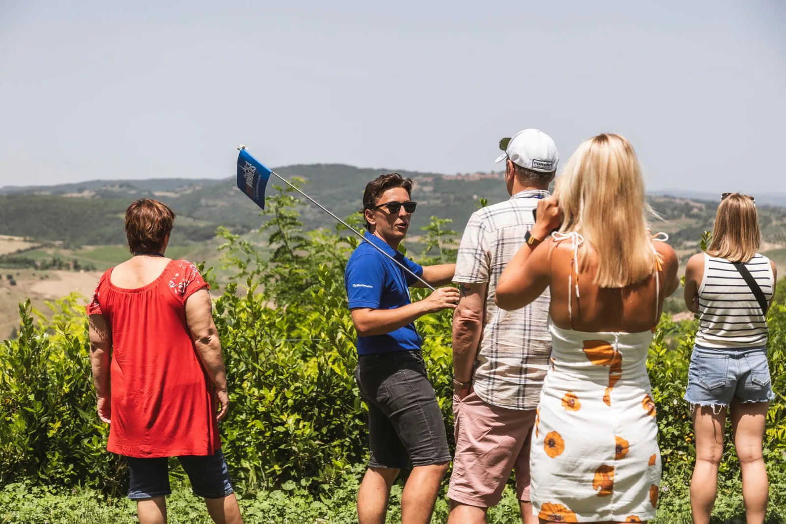 Guide with flag talking to a group of visitors looking out over Tuscan hills
