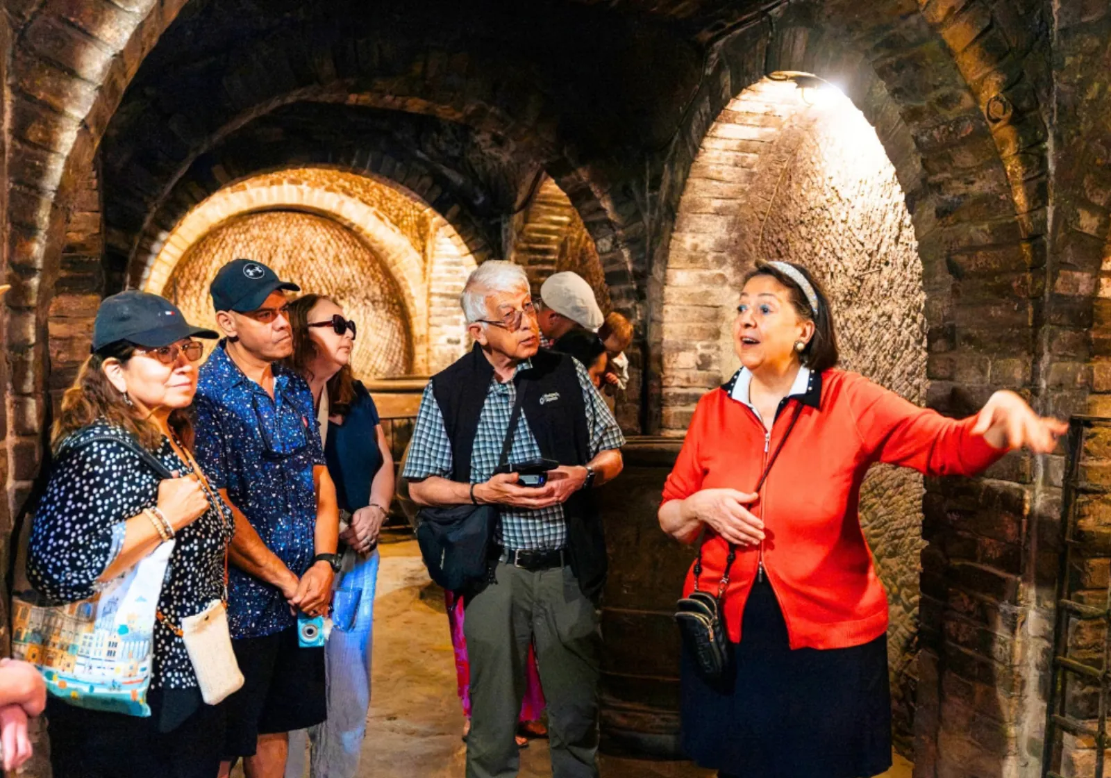 Guide gesturing to a small group inside a brick-vaulted wine cellar