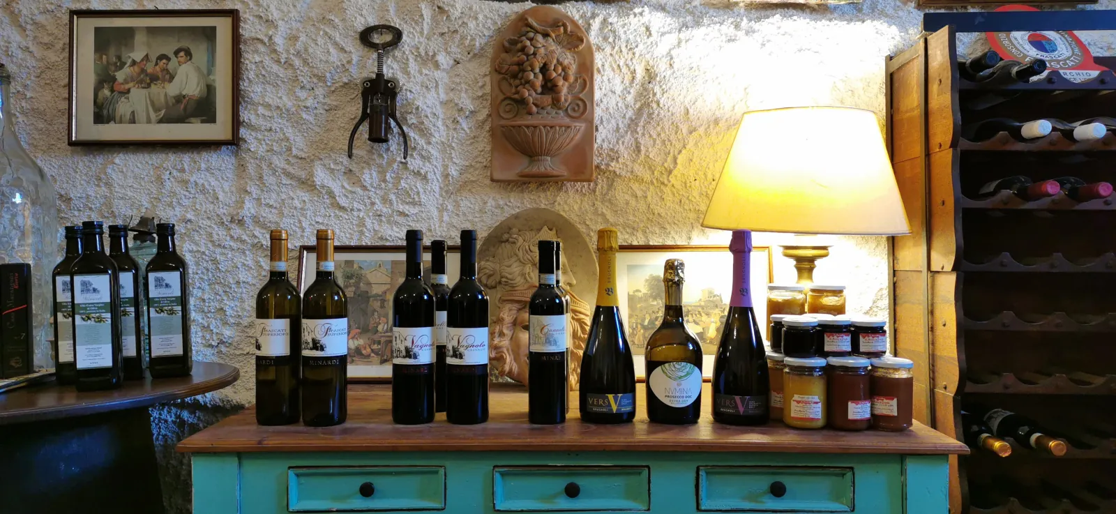 Bottles of olive oil, wine and sparkling wine on a turquoise sideboard in a whitewashed cellar