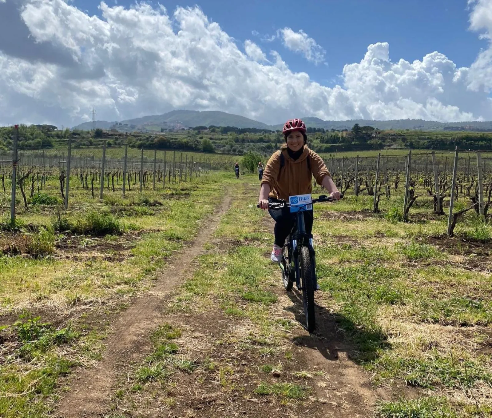 Cyclist on an e-bike riding a dirt track between bare vine rows