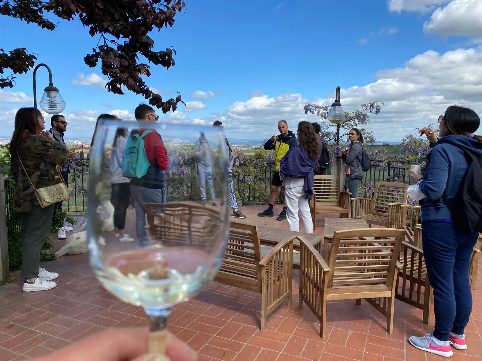 Visitors on a terrace with wicker chairs, a white wine glass in the foreground
