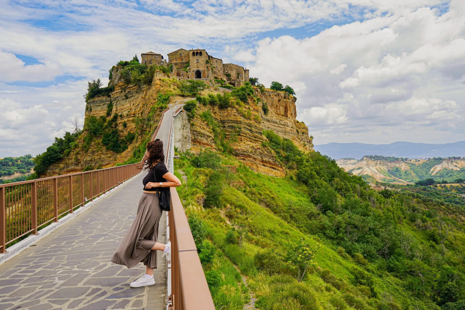 Woman leaning on the railing of the stone footbridge leading to Civita di Bagnoregio