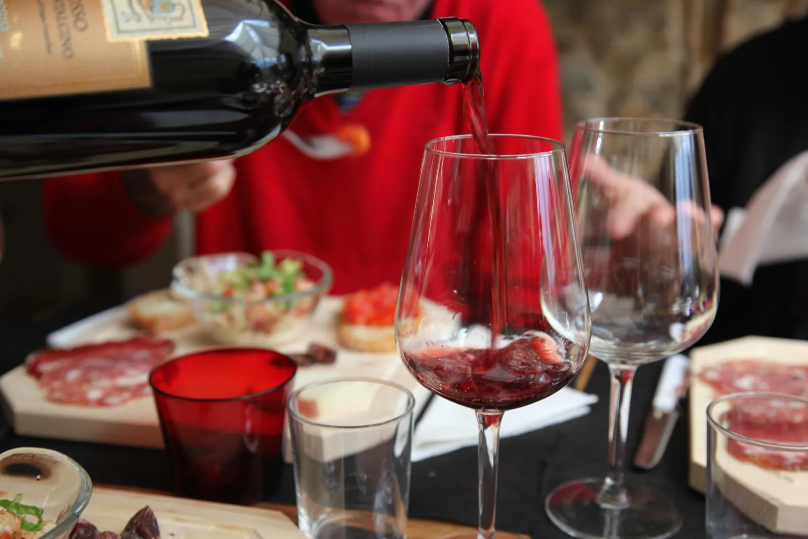Red wine poured into a glass beside plates of cured meat and bruschetta
