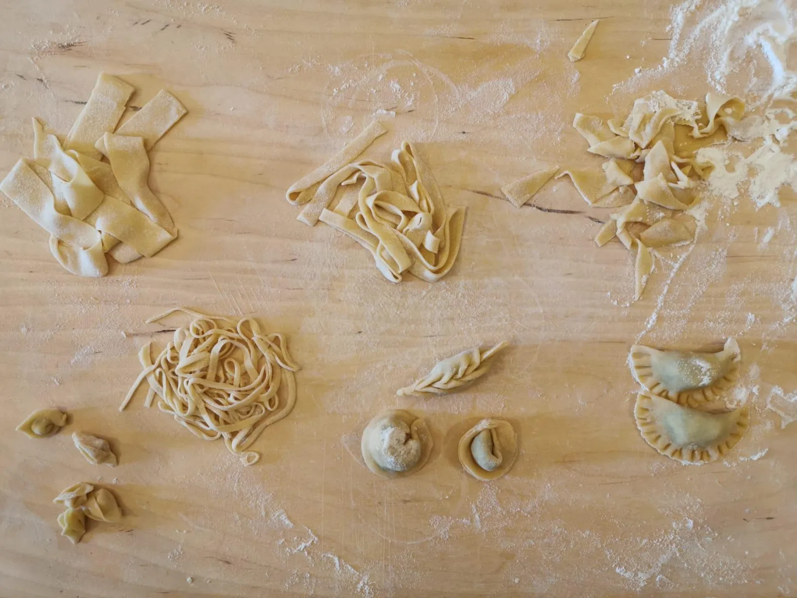 Assorted handmade pasta shapes including tagliatelle, tortellini and filled half-moons on a floured board