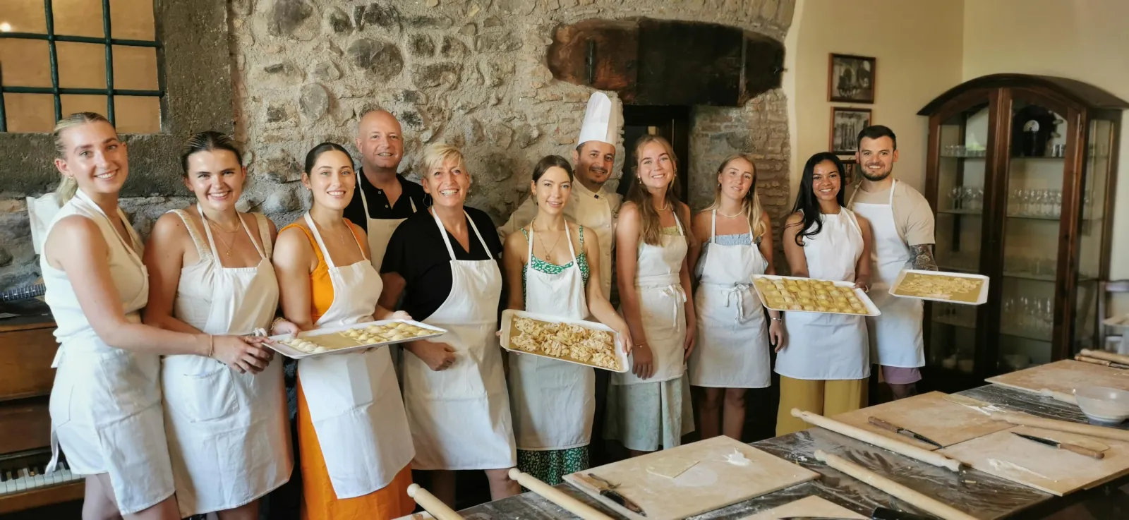 Aproned group with trays of fresh pasta in a stone farmhouse kitchen with a chef