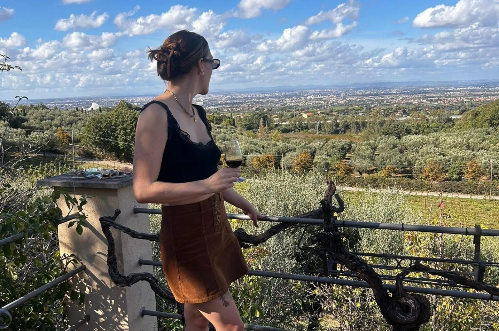 Woman holding red wine on a terrace overlooking olive trees and a wide plain