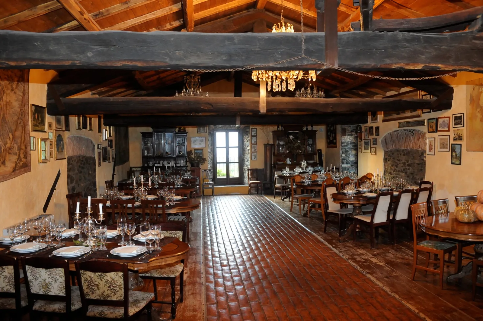 Long set tables in a beam-ceilinged farmhouse dining hall with a chandelier