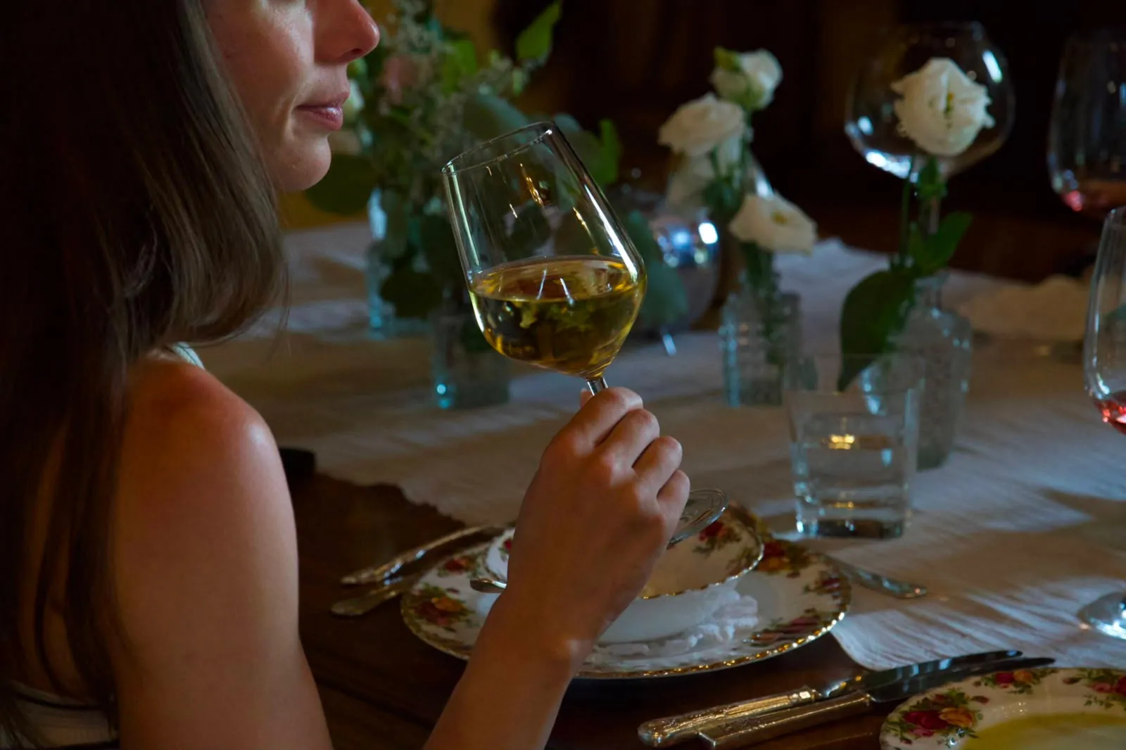 Woman sniffing a glass of white wine at a table with white roses
