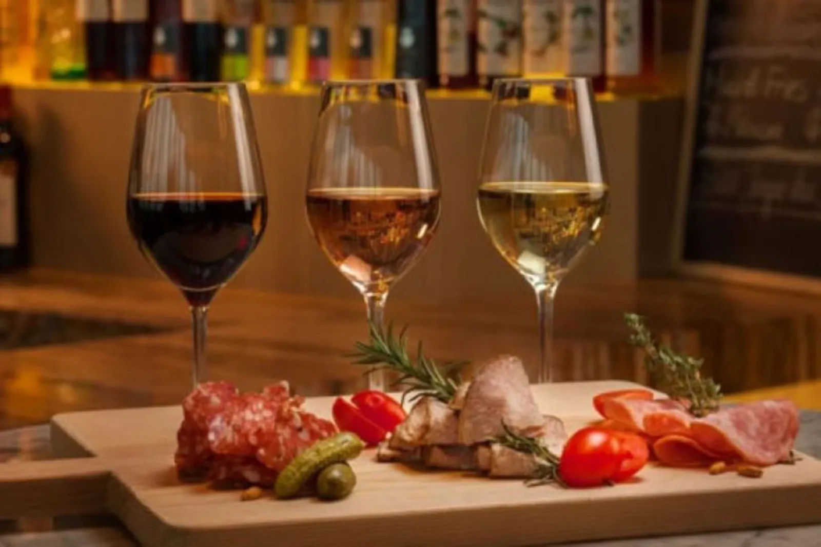 Three glasses of red, rosé and white wine above a board of cured meats and tomatoes