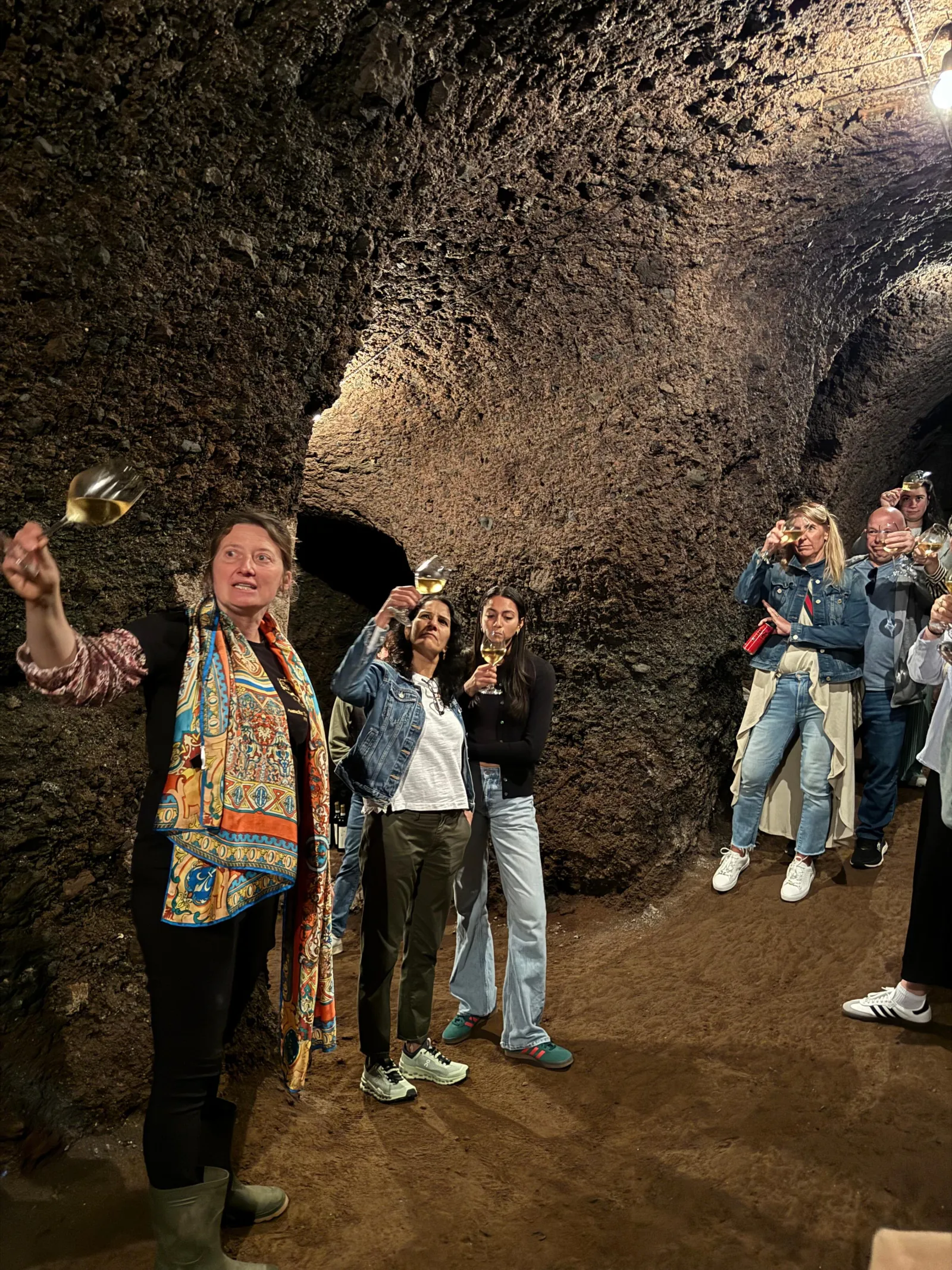 Guide raising a glass in a tufa cave cellar with a group of visitors
