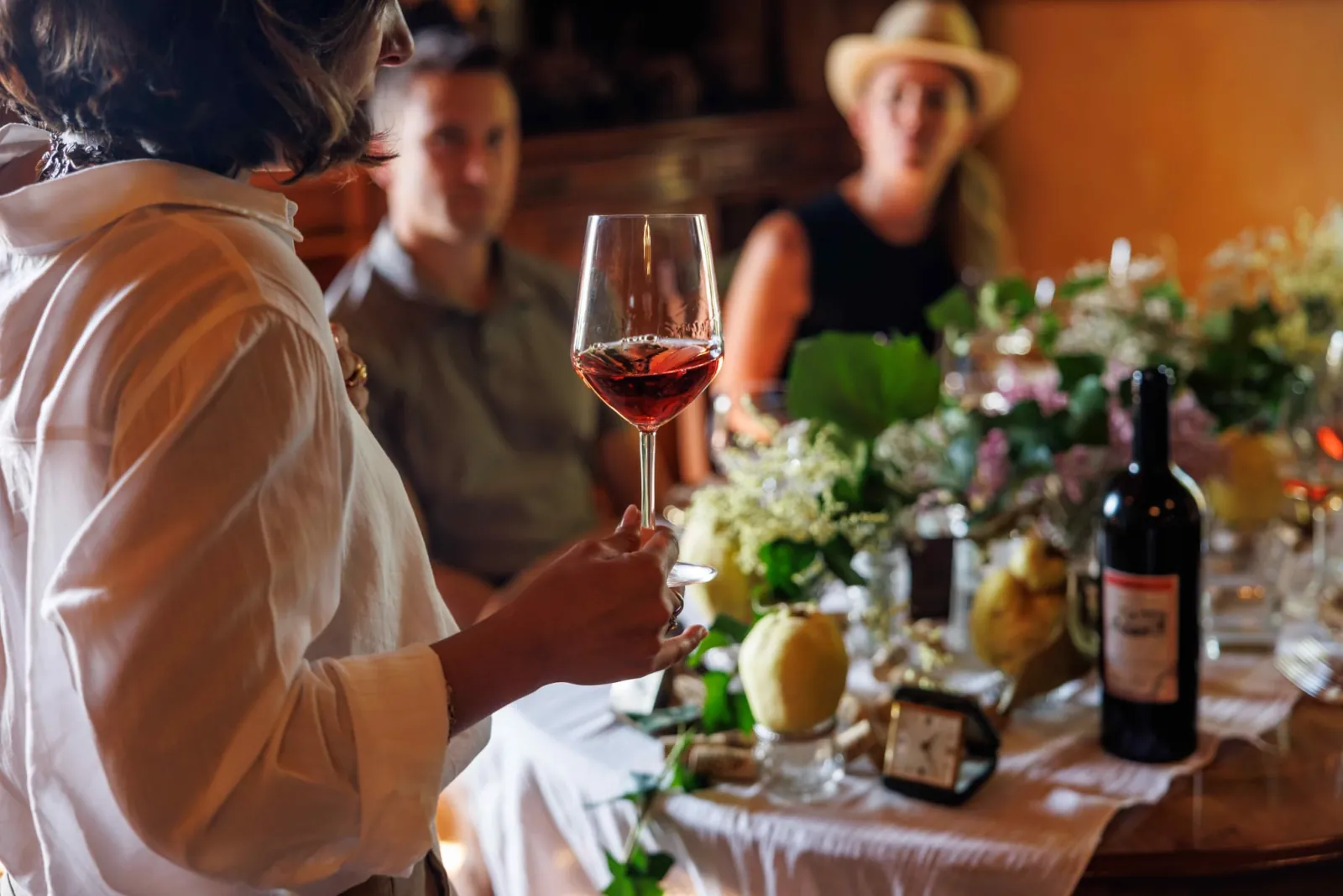 Woman holding a glass of rosé at a table set with flowers and a wine bottle
