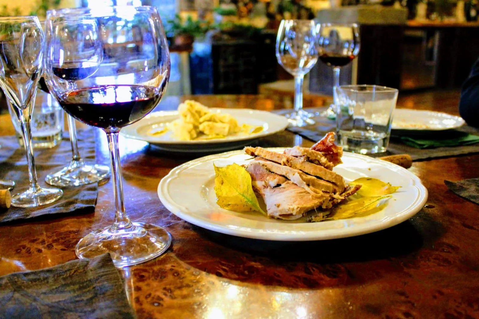 Plate of sliced roast meat with glasses of red wine on a polished wooden table
