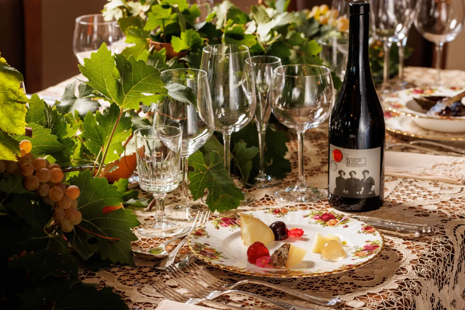 Table with a red wine bottle, cheese plate, wine glasses and vine leaf decoration