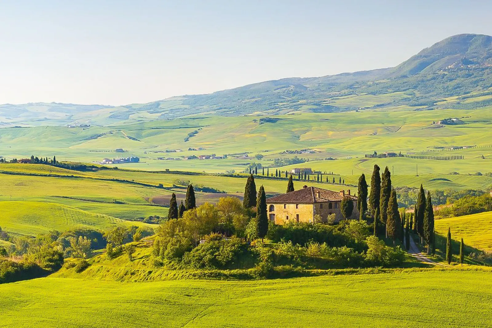 Stone farmhouse among cypresses on rolling green Tuscan farmland