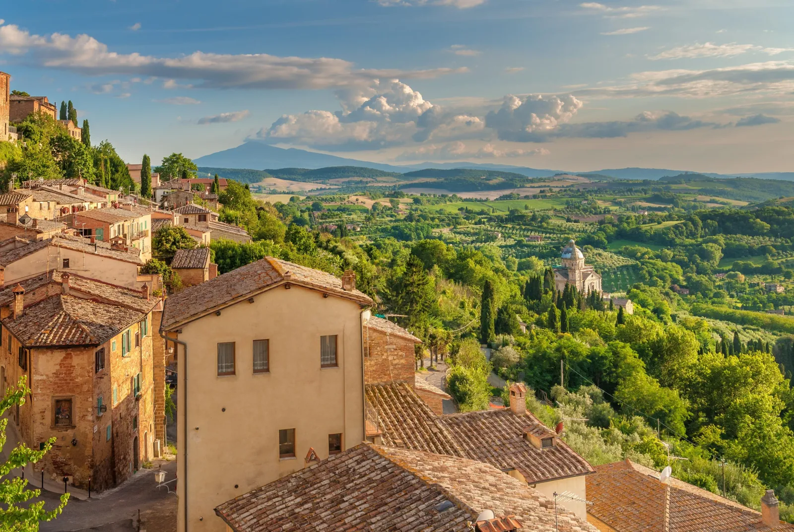 Montepulciano rooftops above green valleys, with the domed San Biagio church in the distance