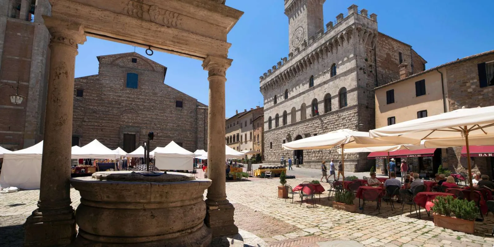 Stone well and market stalls on a hilltop square beside a turreted town hall