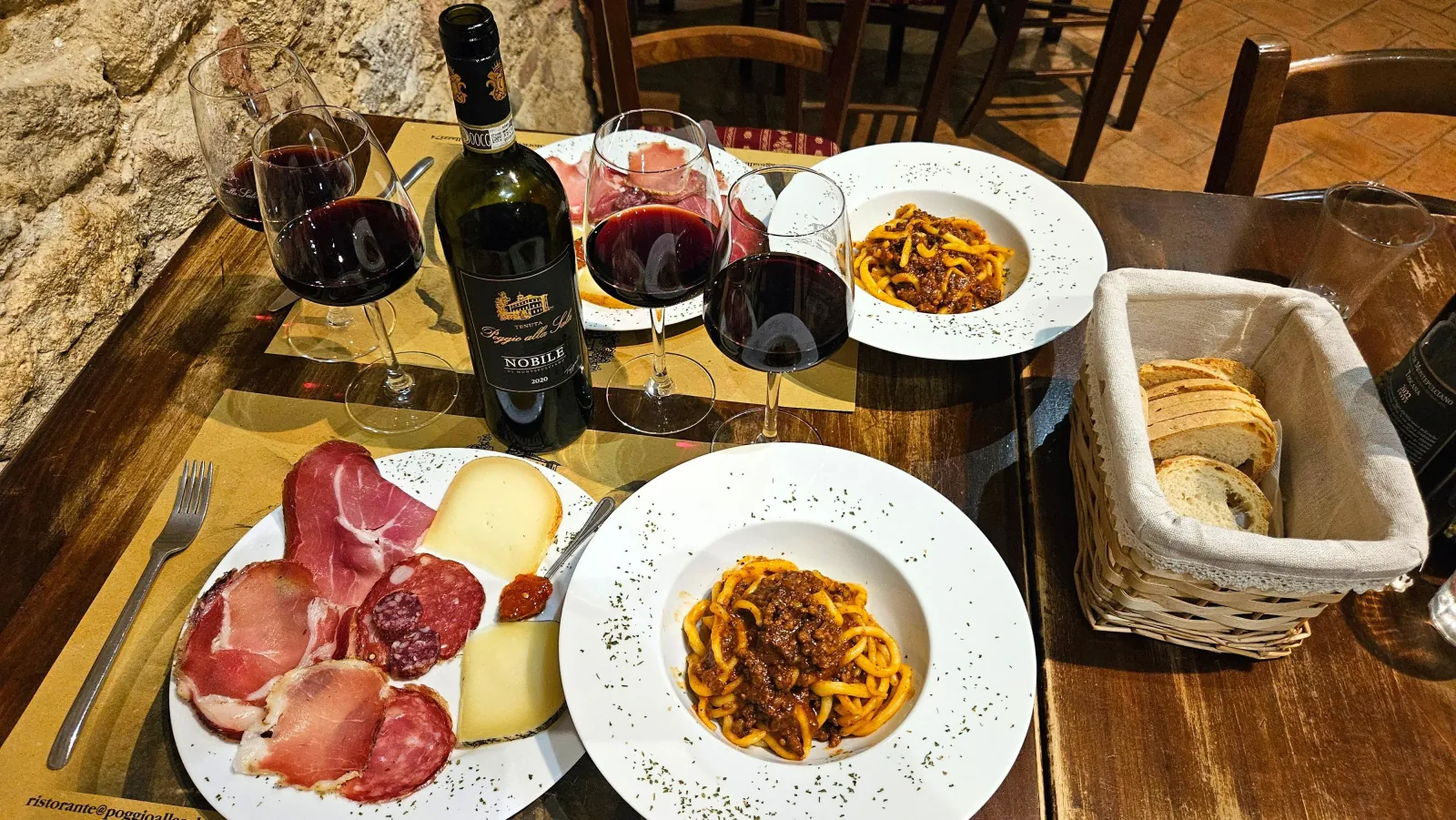 Restaurant table with cured meats, cheese, two pasta plates, bread and glasses of red wine