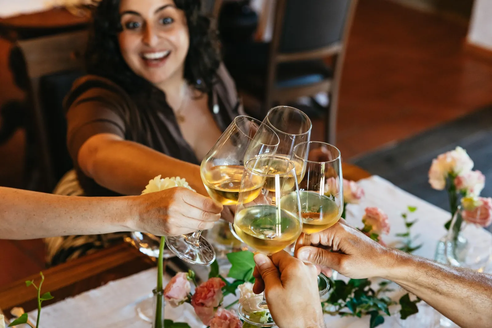 Friends clinking glasses of white wine over a table with pink flowers