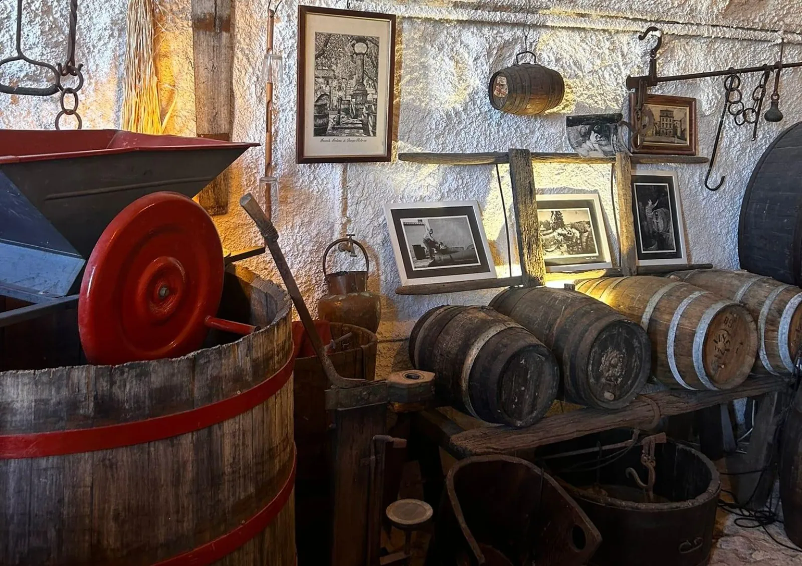 Antique wooden wine press and small barrels against a whitewashed cellar wall with old framed photos