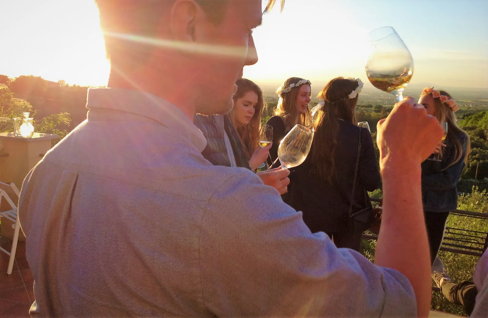 Guests in flower crowns sipping white wine at sunset on a hillside terrace