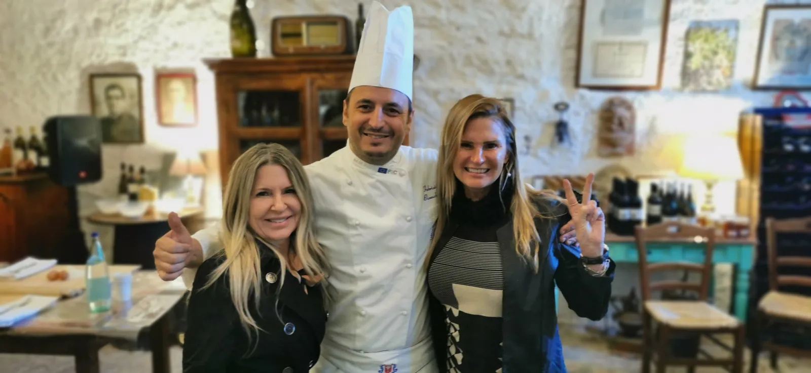 Chef in whites posing with two women in a rustic farmhouse dining room