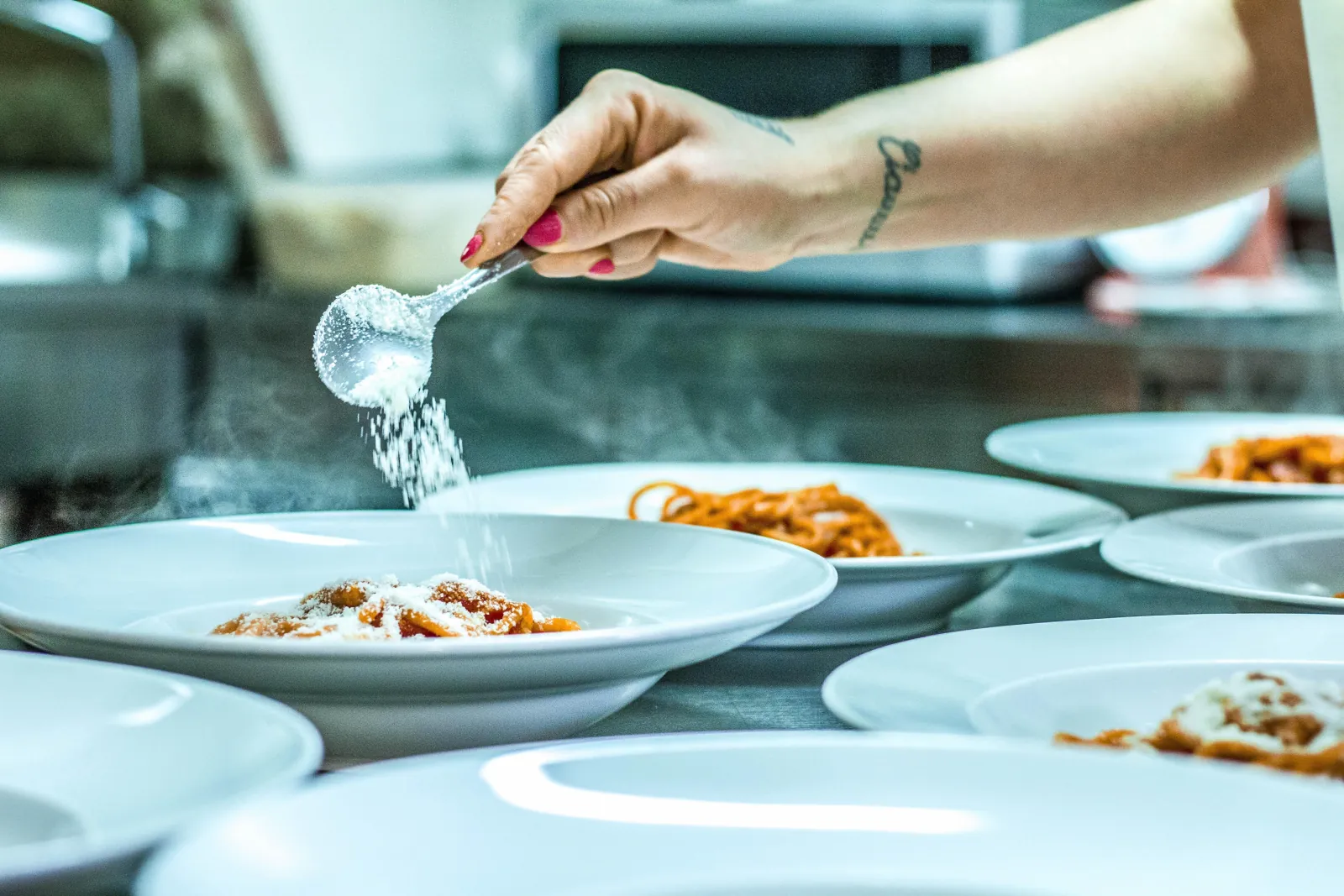 Hand sprinkling grated cheese over plates of tomato pasta in a kitchen